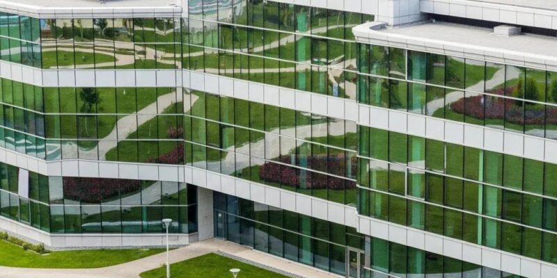Modern energy-efficient building with reflective glass facade, surrounded by greenery, emphasizing indoor air quality and sustainable design principles.